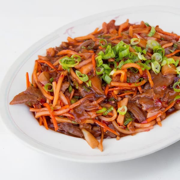 Close-up of a Chinese dish with sliced meat, carrots, and mushrooms, garnished with green onions.