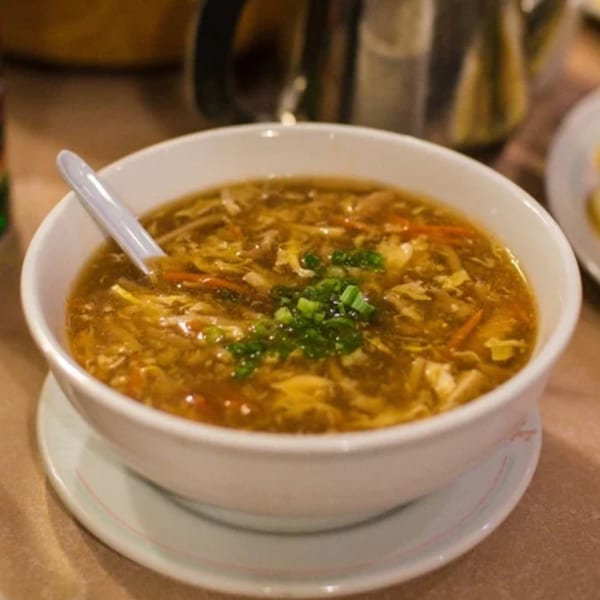 A white bowl of hot and sour soup with scallions and a spoon on a table.
