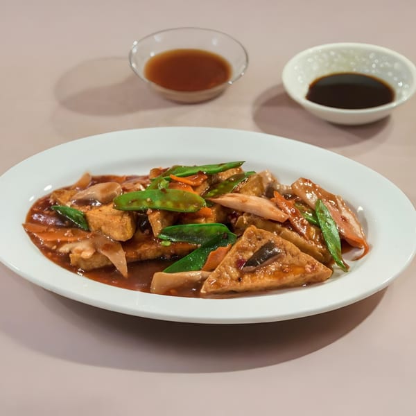 Chinese stir-fried tofu with snow peas, carrots, and mushrooms in a savory brown sauce on a white plate.