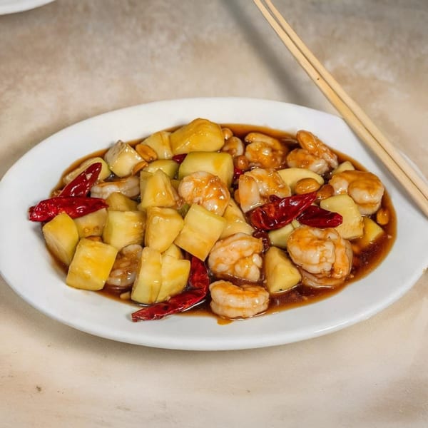 Sweet and sour shrimp with pineapple chunks, red chilies, and peanuts on a white plate.