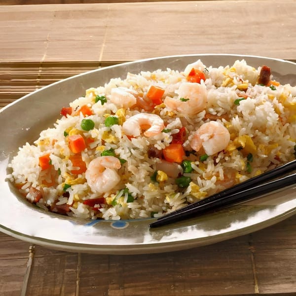 Shrimp fried rice with peas, carrots, and scrambled egg, served on a white oval plate with chopsticks.