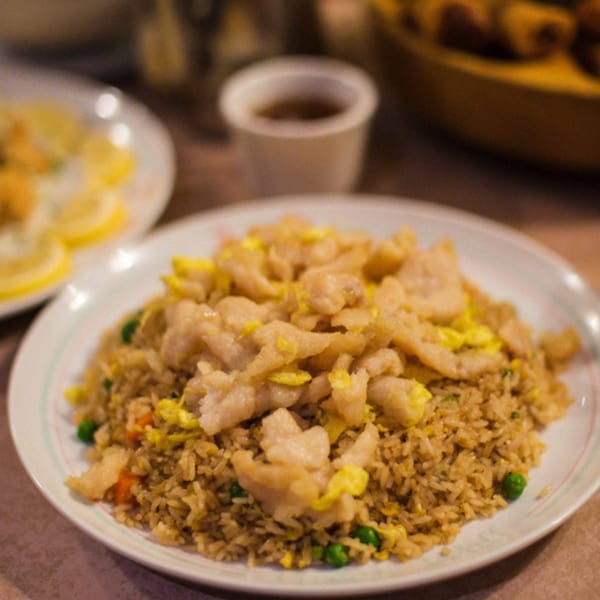A plate of Great Wall Restaurant's fried rice with chicken and peas, with lemon slices in the background.