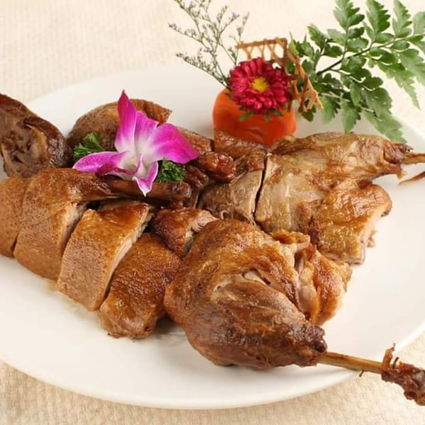 Roasted duck, sliced and whole, garnished with an orchid and greens on a white plate.