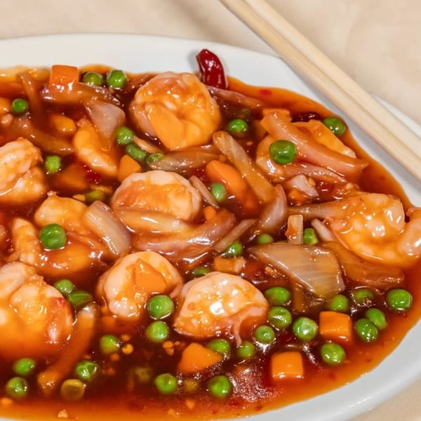 Sweet and sour shrimp with peas, carrots, and onions, served on a white plate with chopsticks.