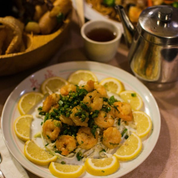 A plate of Great Wall Restaurant's fried shrimp with green onions and lemon slices, with tea in the background.
