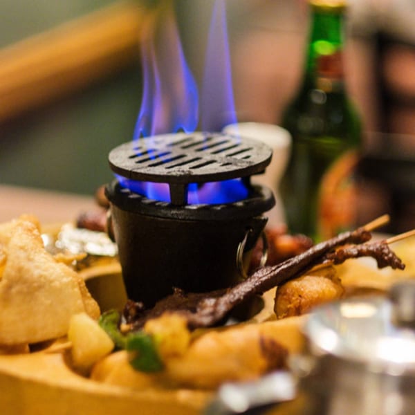 Chinese appetizer platter with fried items, skewers, and a small grill with blue flames.